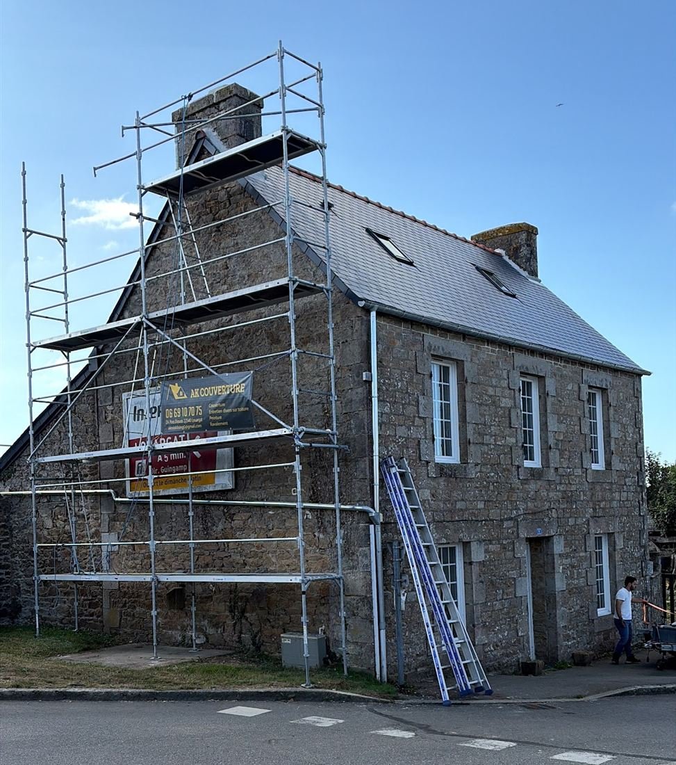 Maison en pierre couverte d’ardoise, échafaudage monté contre le pignon avec la bâche AK Couverture