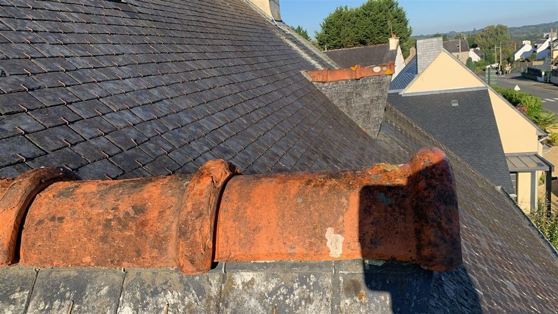 Tuiles faîtières en terre cuite scellées au sommet d’un toit en ardoise